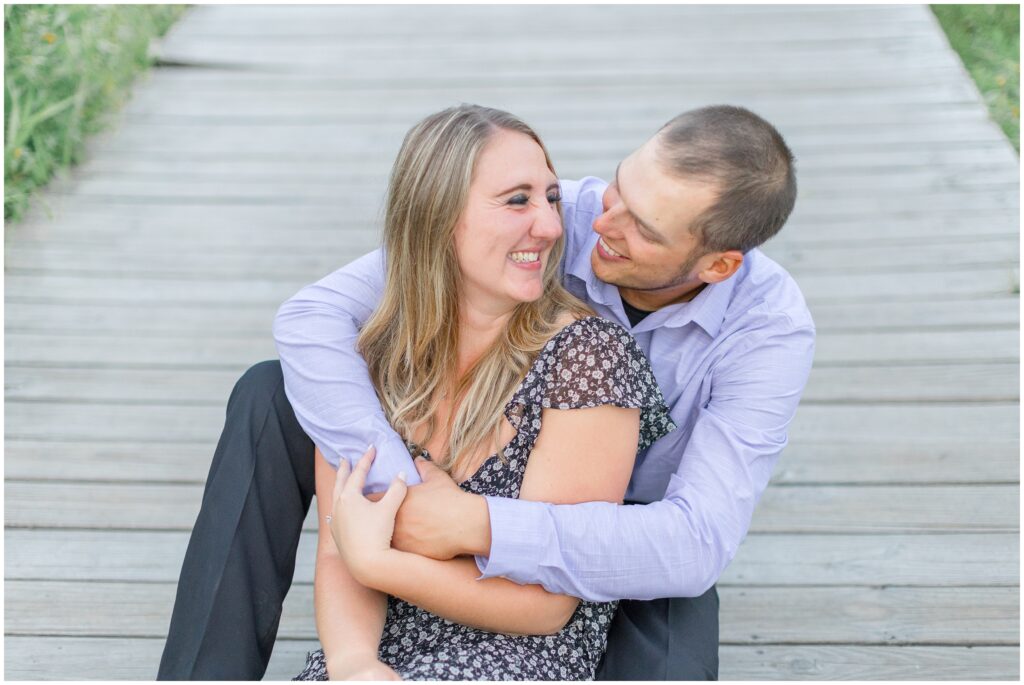 Couple laughing together and hugging sitting on a boardwalk for their lion's den gorge engagement session.