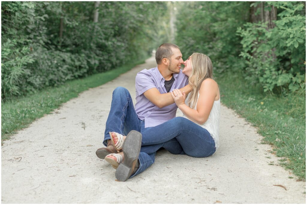 Couple almost kissing, sitting on a path for their lion's den gorge engagement session.